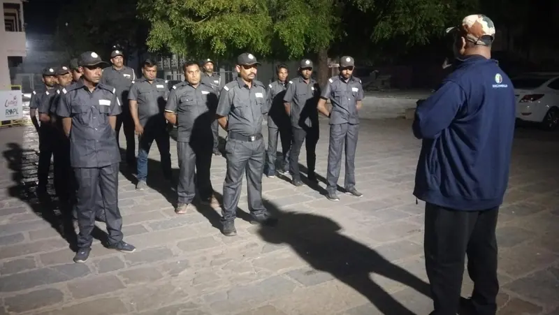 A GHS team leader briefing a line of guards in grey uniforms at night